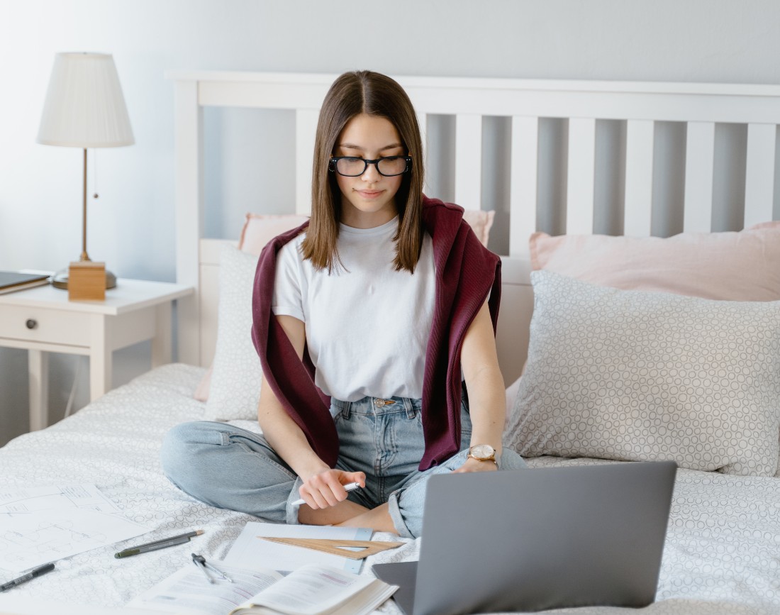 Fata care studiaza in pat de pe un laptop